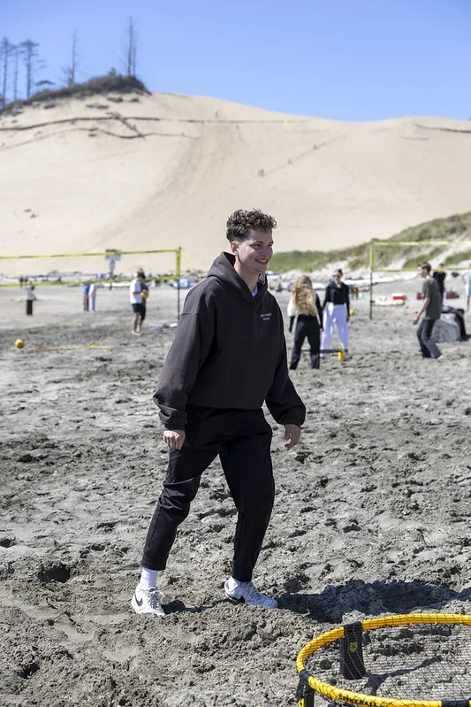 A young man mid-game on the sand at the youth beach trip, with a huge dune and volleyball nets behind him